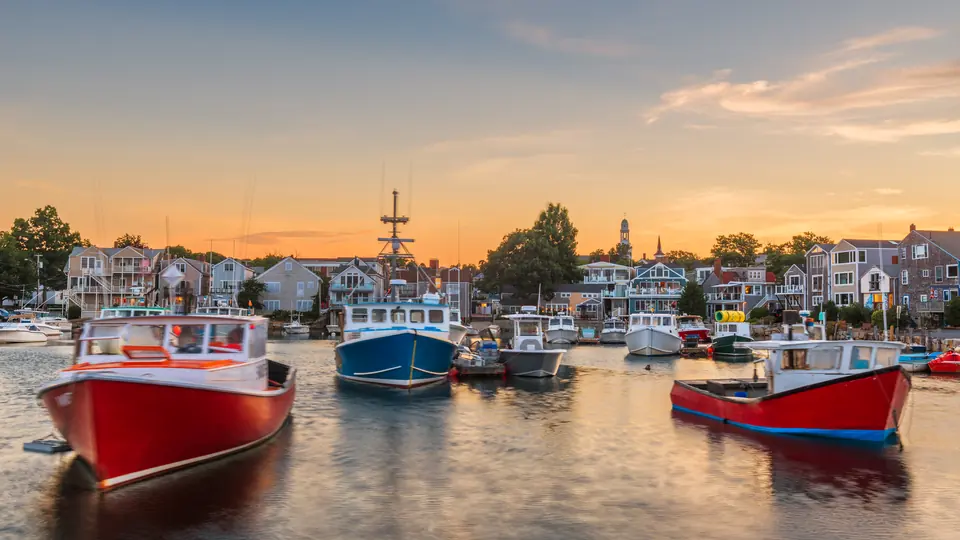 Rockport harbor at sunset with lobster boats and shoreline homes.