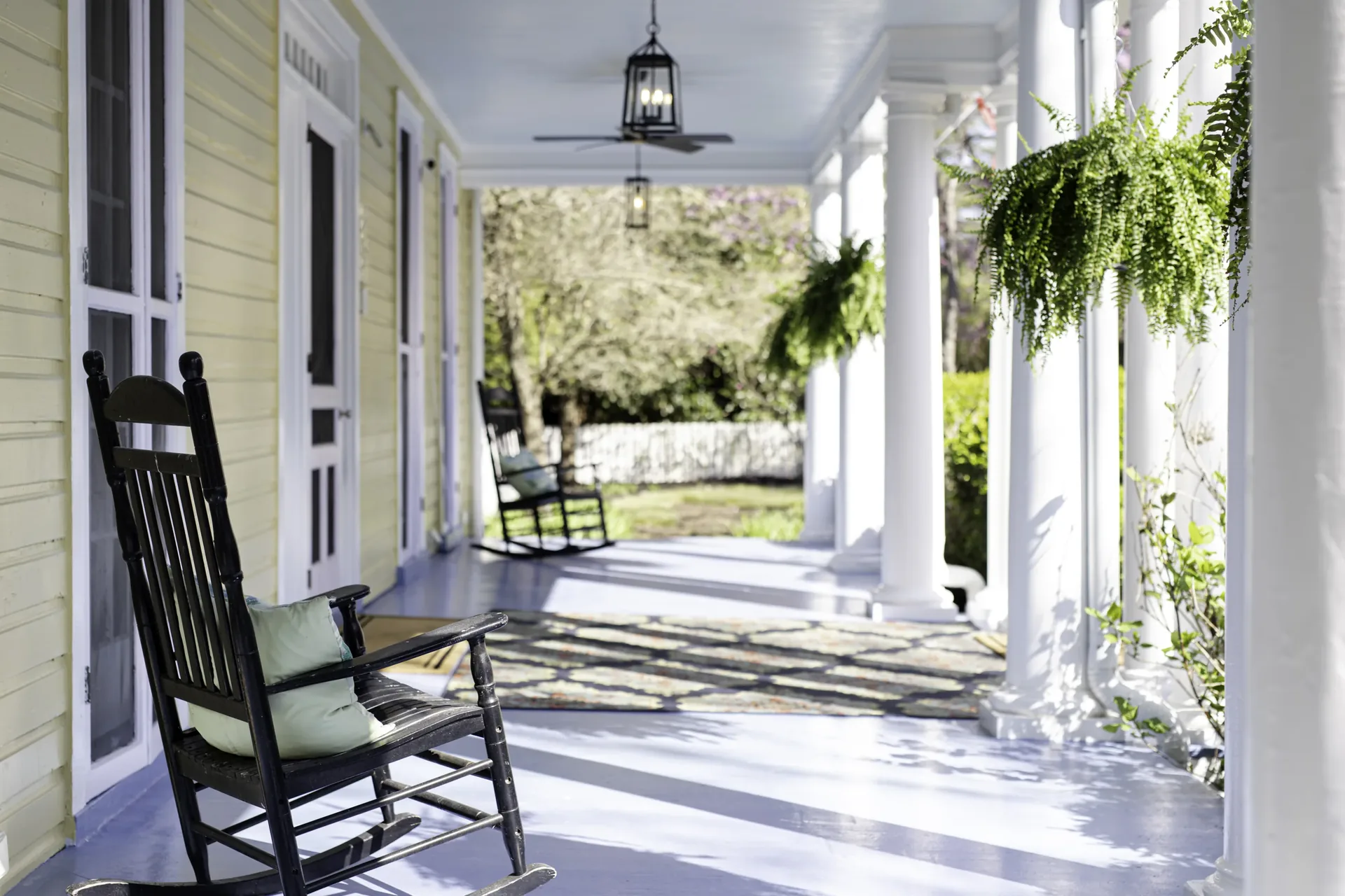 A New England porch with rocking chairs and hanging ferns in morning light