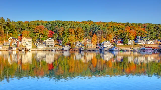 Brightly painted New Hampshire waterfront houses reflected in still lake water at peak fall foliage