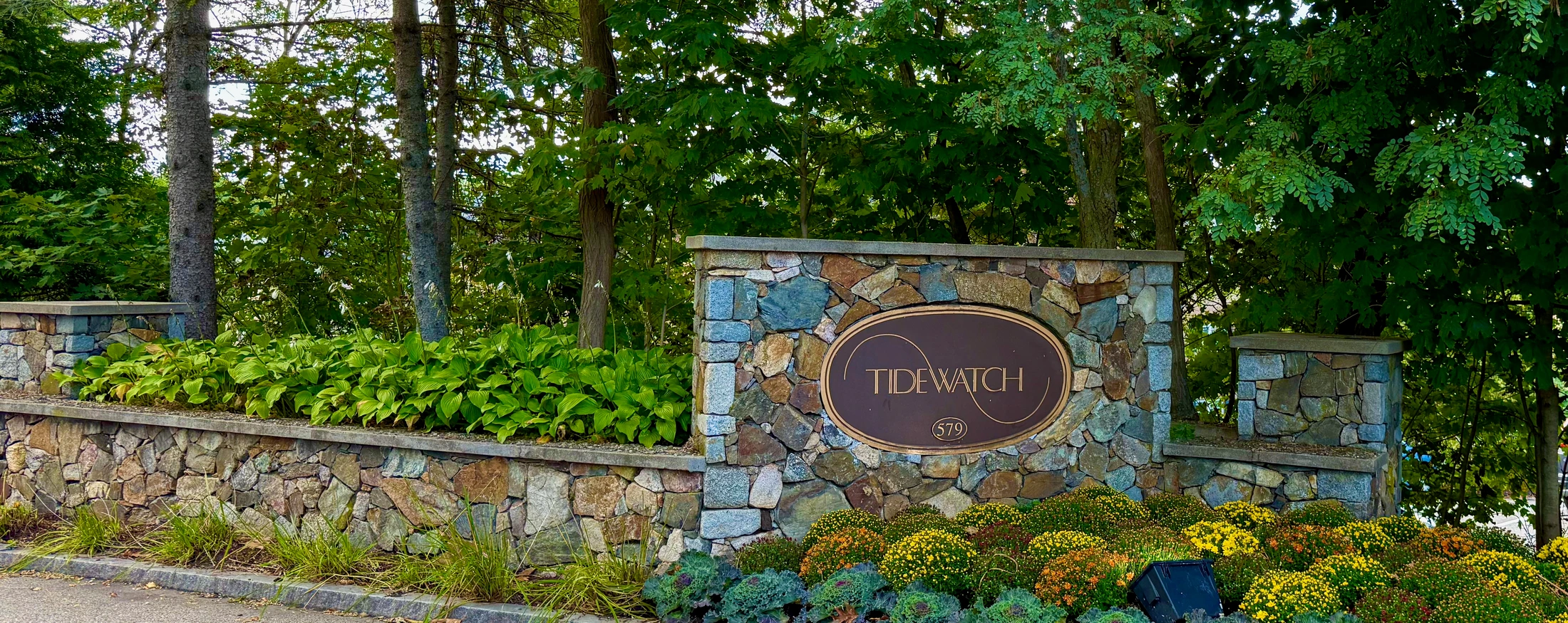 Tidewatch entrance monument at 579 Sagamore Avenue, surrounded by stone walls, flowers and mature trees